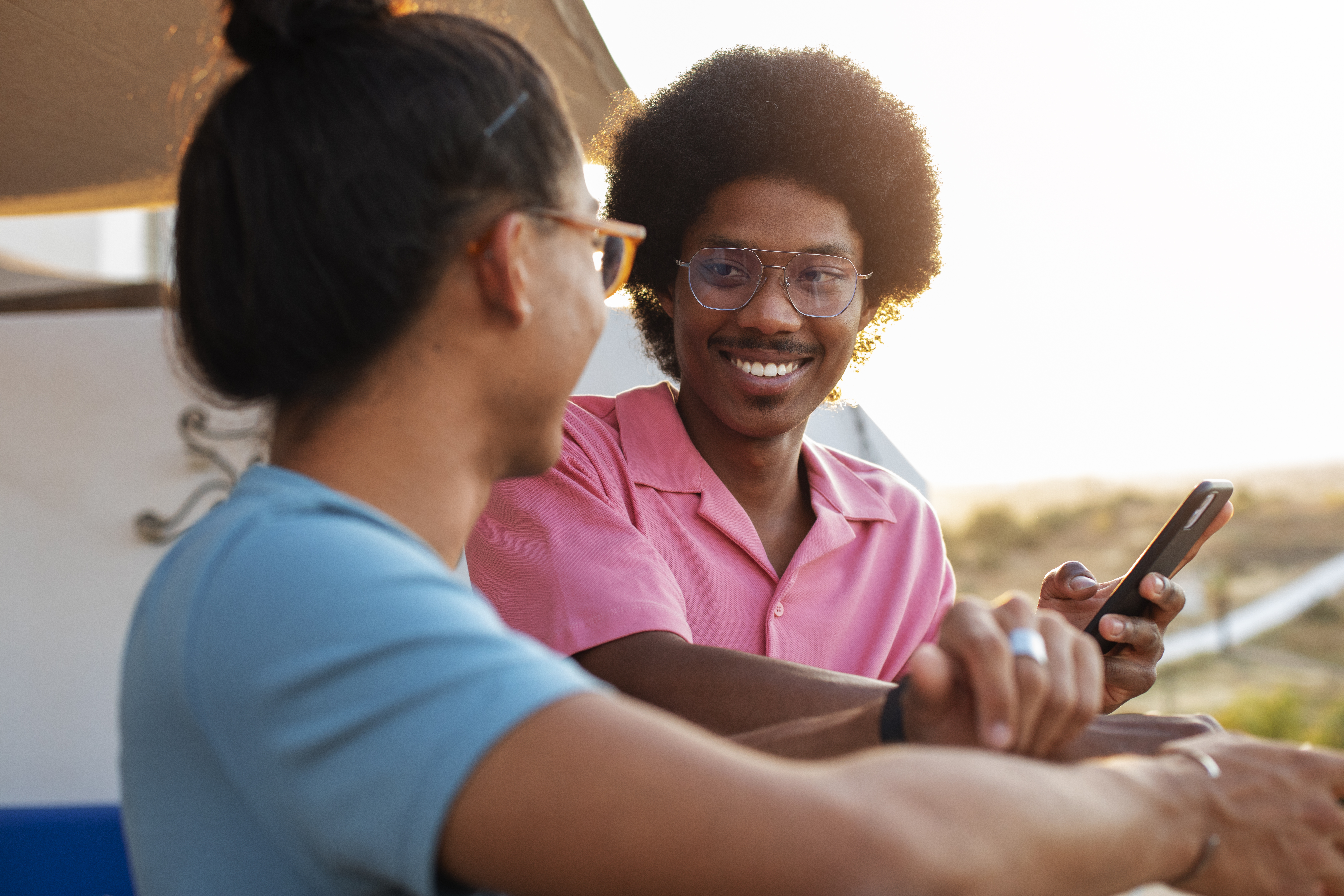 Two friends smiling at sunset, one using Nawiri on a smartphone